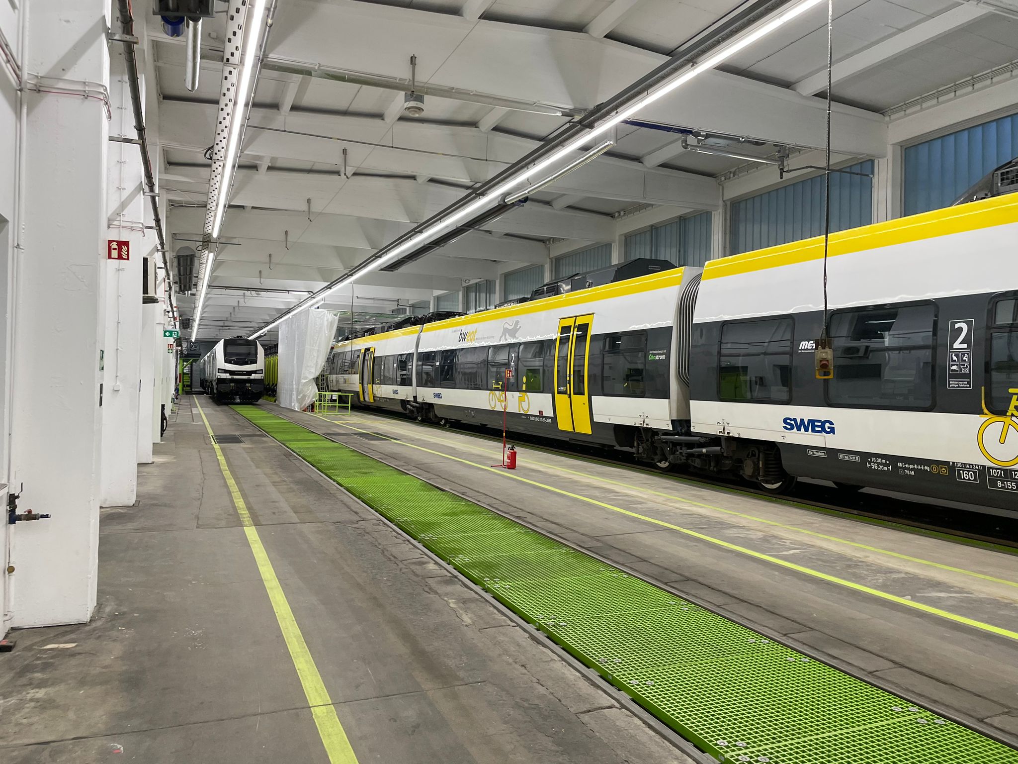Große helle Werkhalle mit Triebzug und Lokomotive auf Gleisen